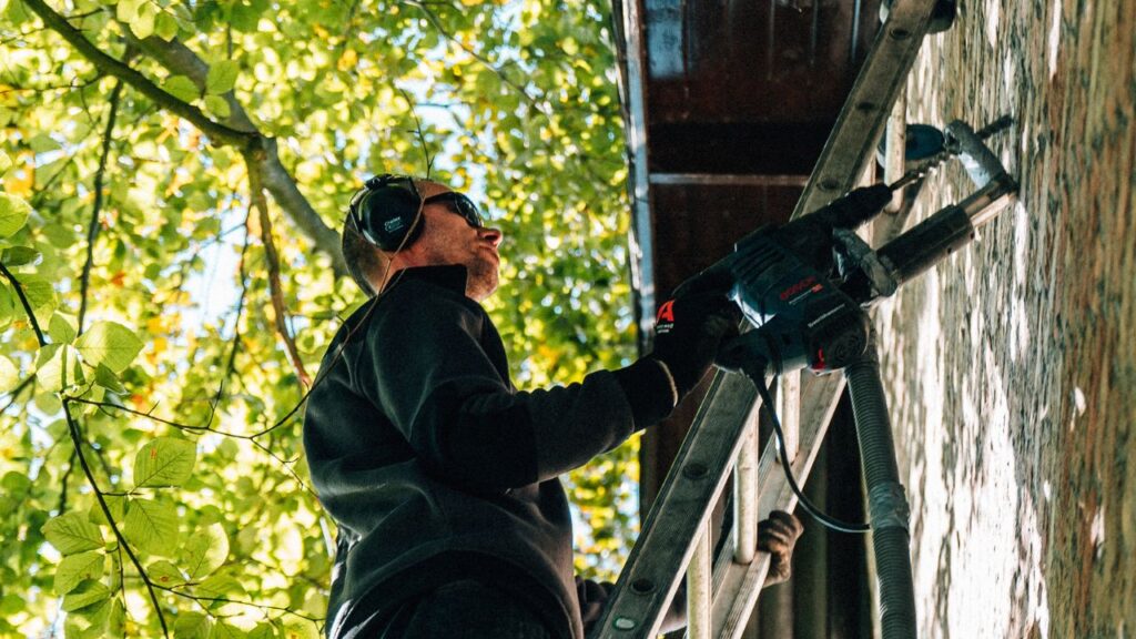Gevelisolatie spouwmuur man op ladder aan het boren